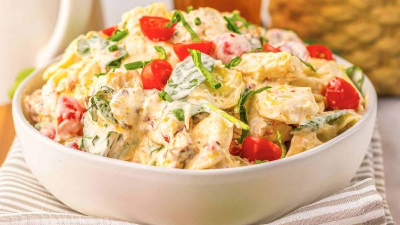 A white bowl filled with creamy pasta salad, mixed with chopped spinach, cherry tomatoes, and a creamy dressing.