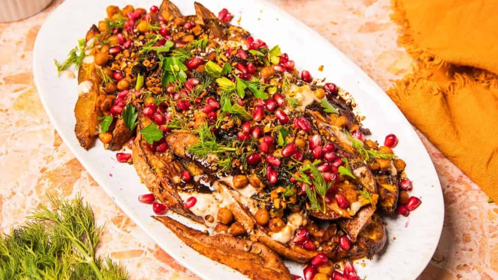 Roasted eggplant topped with chickpeas, pomegranate seeds, herbs, and spices on a white oval plate.