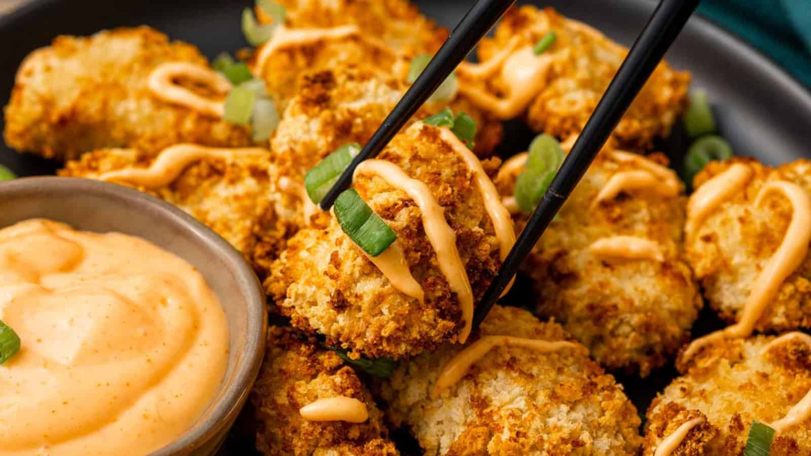 Air fryer bang bang chicken bites coated in creamy spicy sauce and topped with green onions.