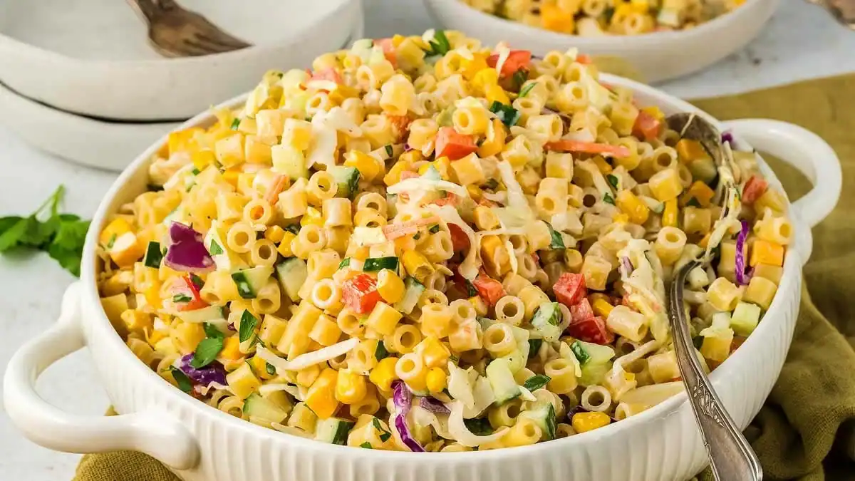 Creamy macaroni salad with diced veggies and cheese in a white bowl with a spoon.