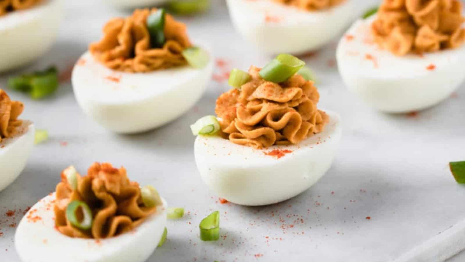 Deviled eggs topped with paprika and chopped green onions on a light surface.