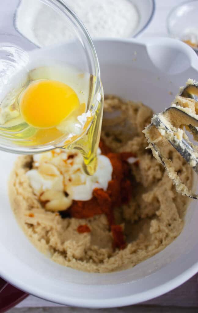 A raw egg is being poured into a mixing bowl with batter and beaters, ready for baking a delicious Pumpkin Cookies Recipe.