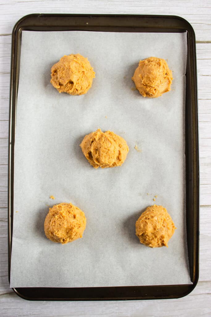 Five scoops of pumpkin cookie dough on a parchment-lined baking sheet, ready to bake—perfect for the ultimate Pumpkin Cookies recipe.