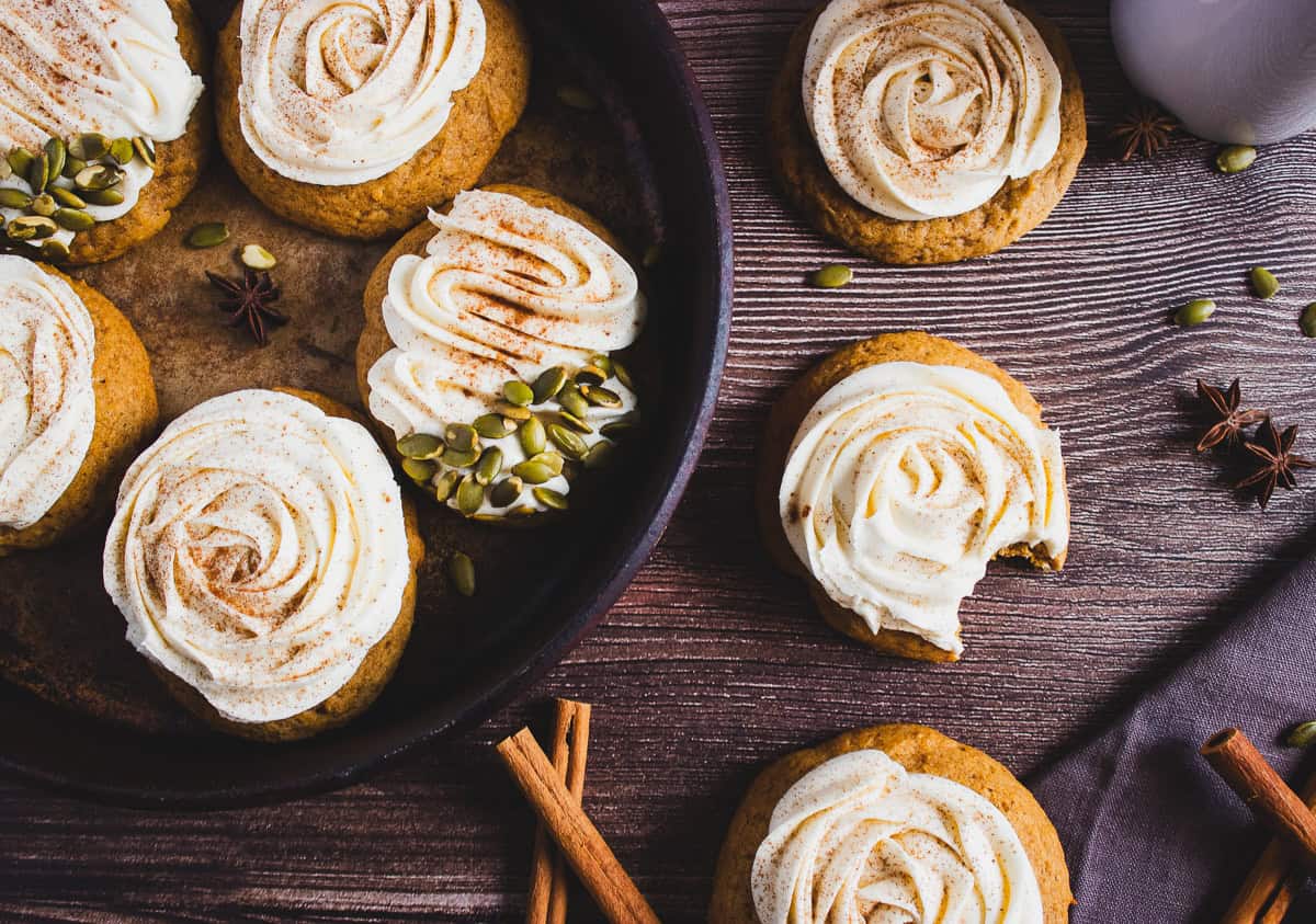 Iced cookies with cinnamon and seeds on a wooden table, one cookie has a bite taken out of it—these delightful treats are inspired by a Pumpkin Cookies recipe and would pair perfectly with rich cream cheese frosting.