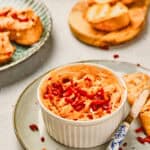 A ramekin of creamy Maple Bacon Cheese Dip topped with chopped red peppers, served with toasted bread slices on the side.