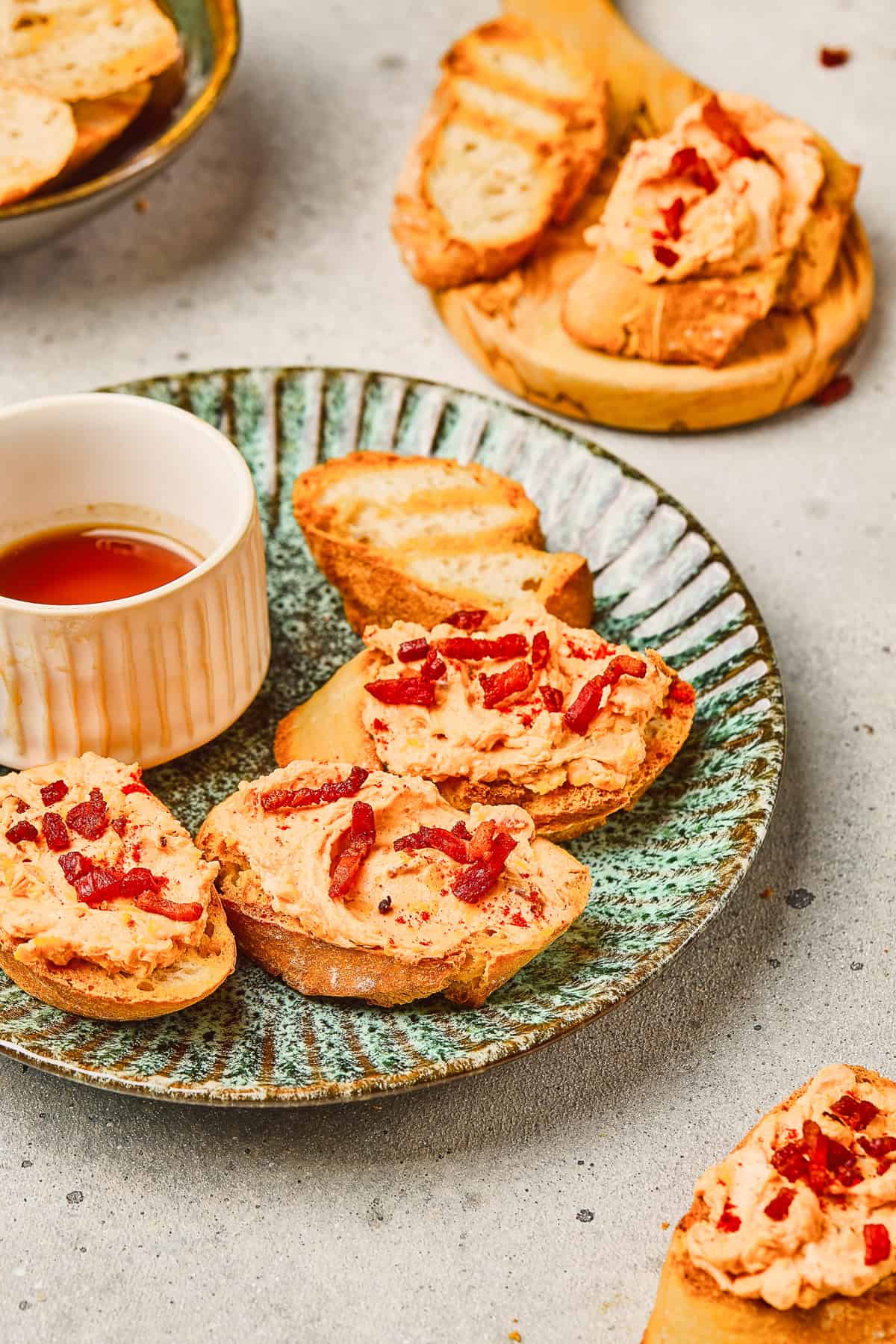 Toasted bread slices topped with creamy spread and chopped red toppings, served with a small cup of Maple Bacon Cheese Dip.