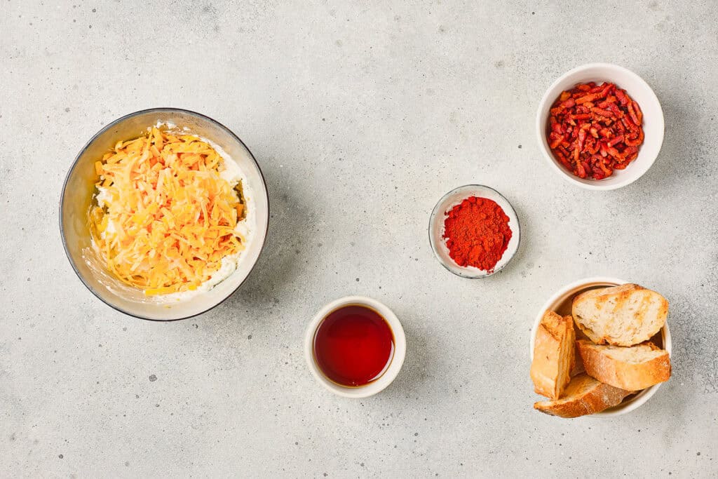 Bowl of Cheese Dip featuring paprika, oil, and savory bacon bits, served with sliced bread on a light-colored surface—a delicious Maple Bacon Cheese Dip perfect for any gathering.