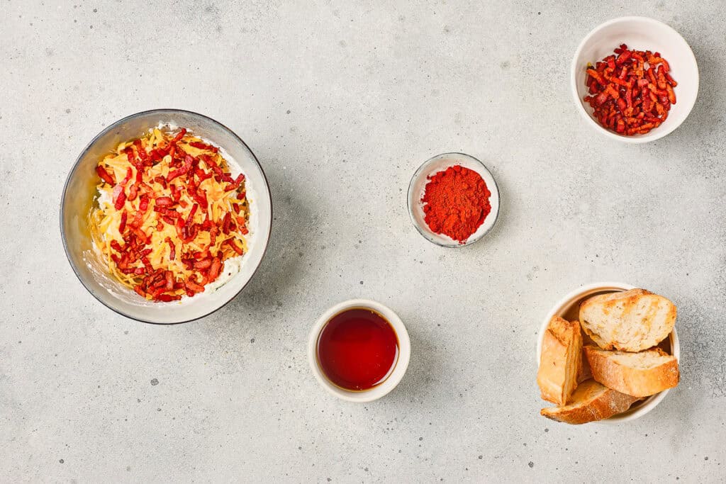 A bowl of rich Maple Bacon Cheese Dip with crispy bacon bits, a hint of paprika, sweet syrup, and toasted bread slices on a light surface.