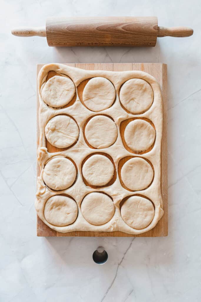 Dough circles cut on a wooden board with a rolling pin and cookie cutter nearby, ready to be transformed into delicious Maple Glazed Donuts.