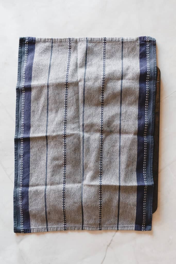 Gray and blue checkered cloth napkin laid flat on a light-colored marble surface, perfect for serving fresh maple donuts or glazed donuts.