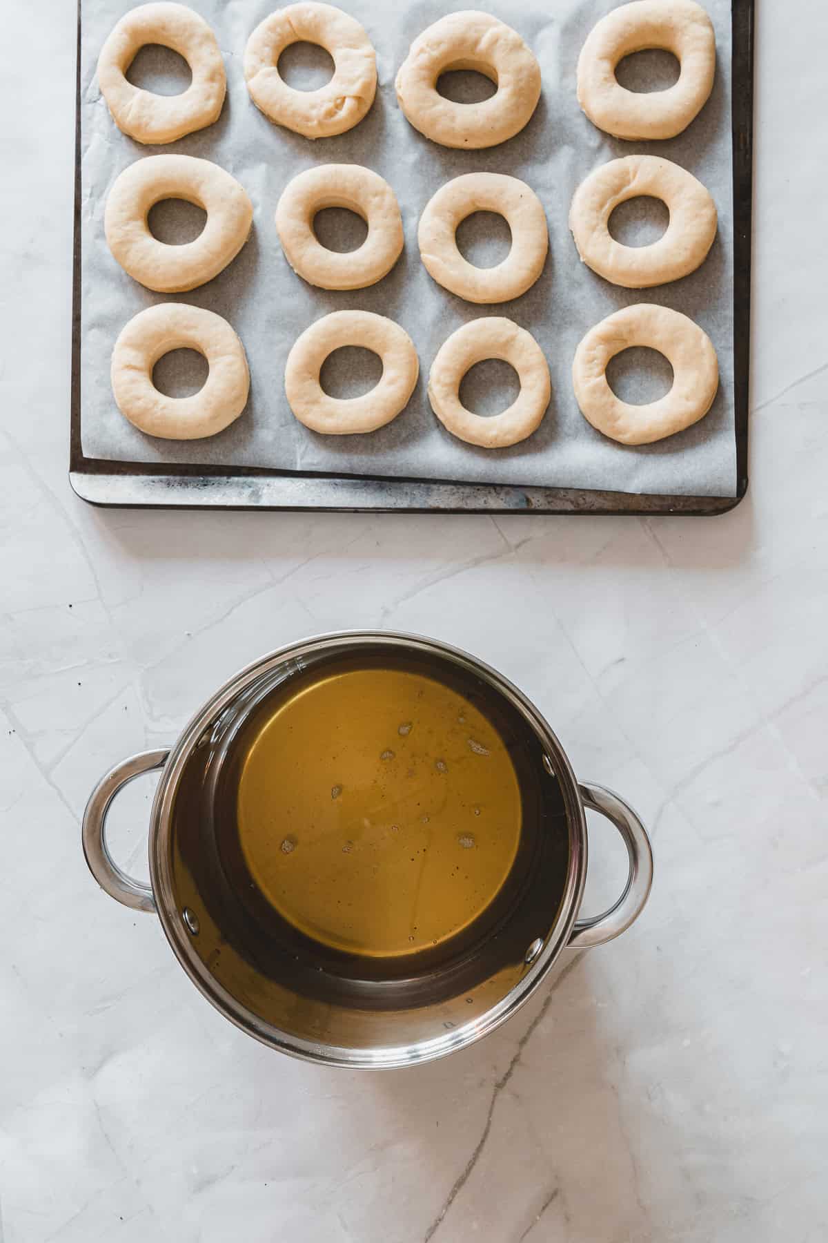 Uncooked donut rings on a tray and a pot of oil on a marble countertop, ready for frying into delicious maple glazed donuts.
