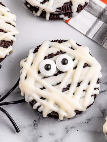 Chocolate cupcakes decorated as mummies with white icing and candy eyes, plus a plastic spider on the side.