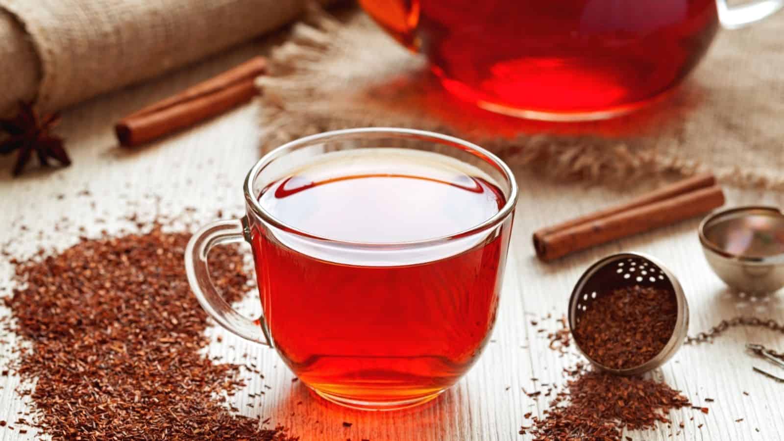 A clear cup of red tea with loose tea leaves, cinnamon sticks, and a tea infuser on a white tableโa delicious way to explore 7 coffee alternatives in your daily routine.