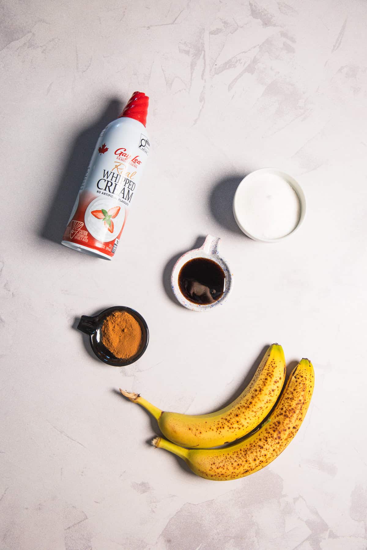 A can of whipped cream, two bananas, and small bowls of powder and syrup for a banana bread latte.