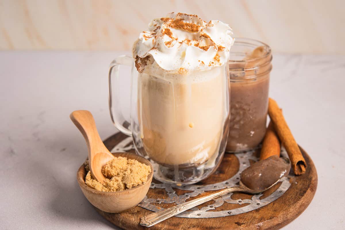 A banana bread latte topped with whipped cream and cinnamon, served with brown sugar and cinnamon sticks.