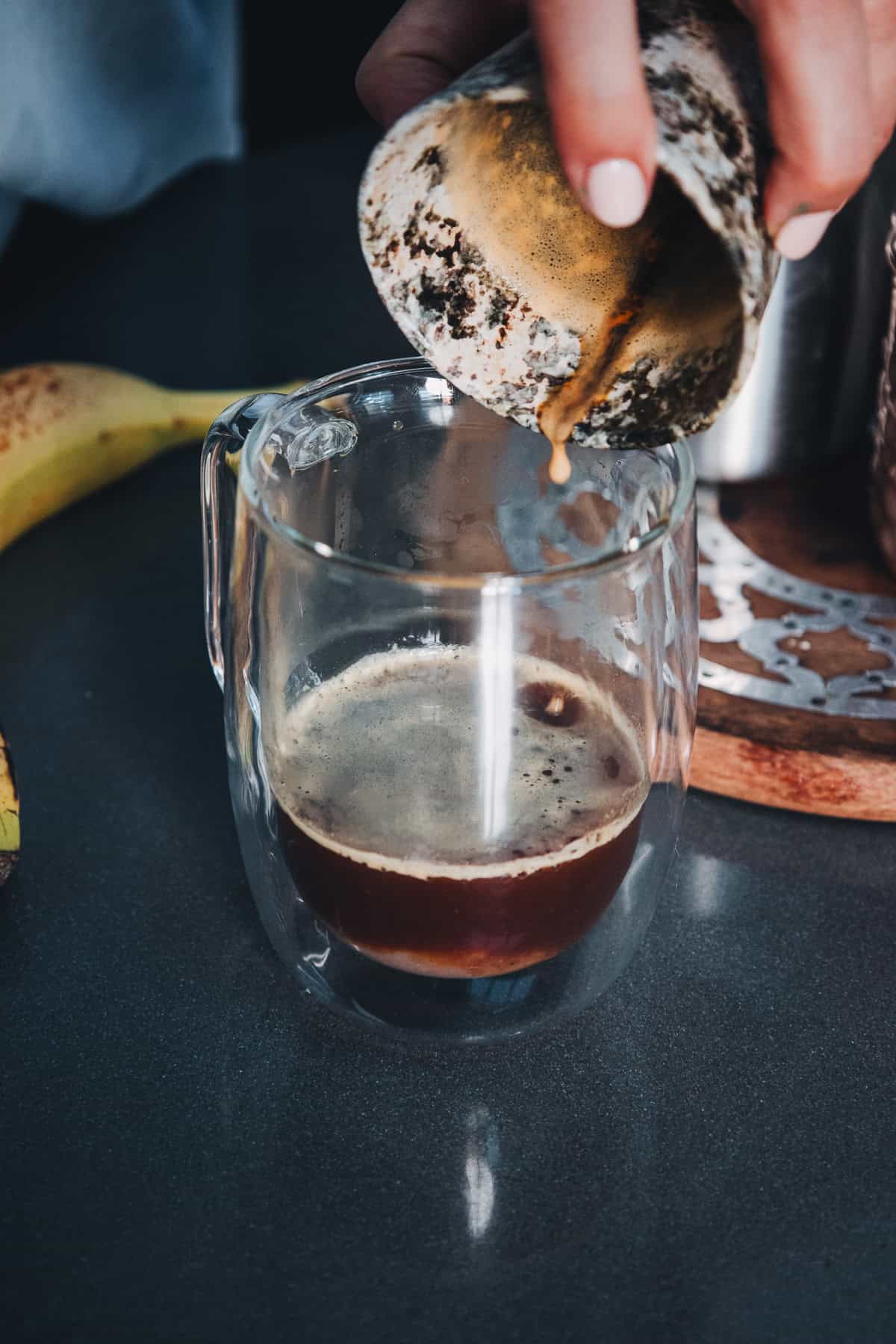 Espresso being poured from a metal portafilter into a glass mug for a banana bread latte.