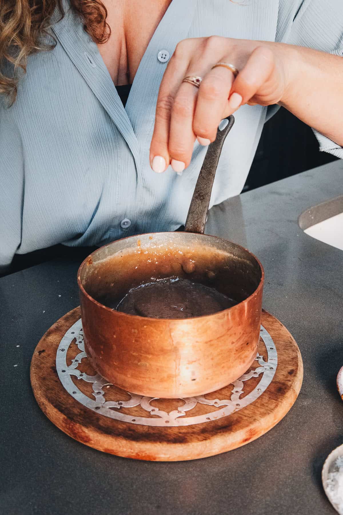 A person sprinkles salt into a small copper pot of melted chocolate for a Starbucks copycat coffee syrup recipe.
