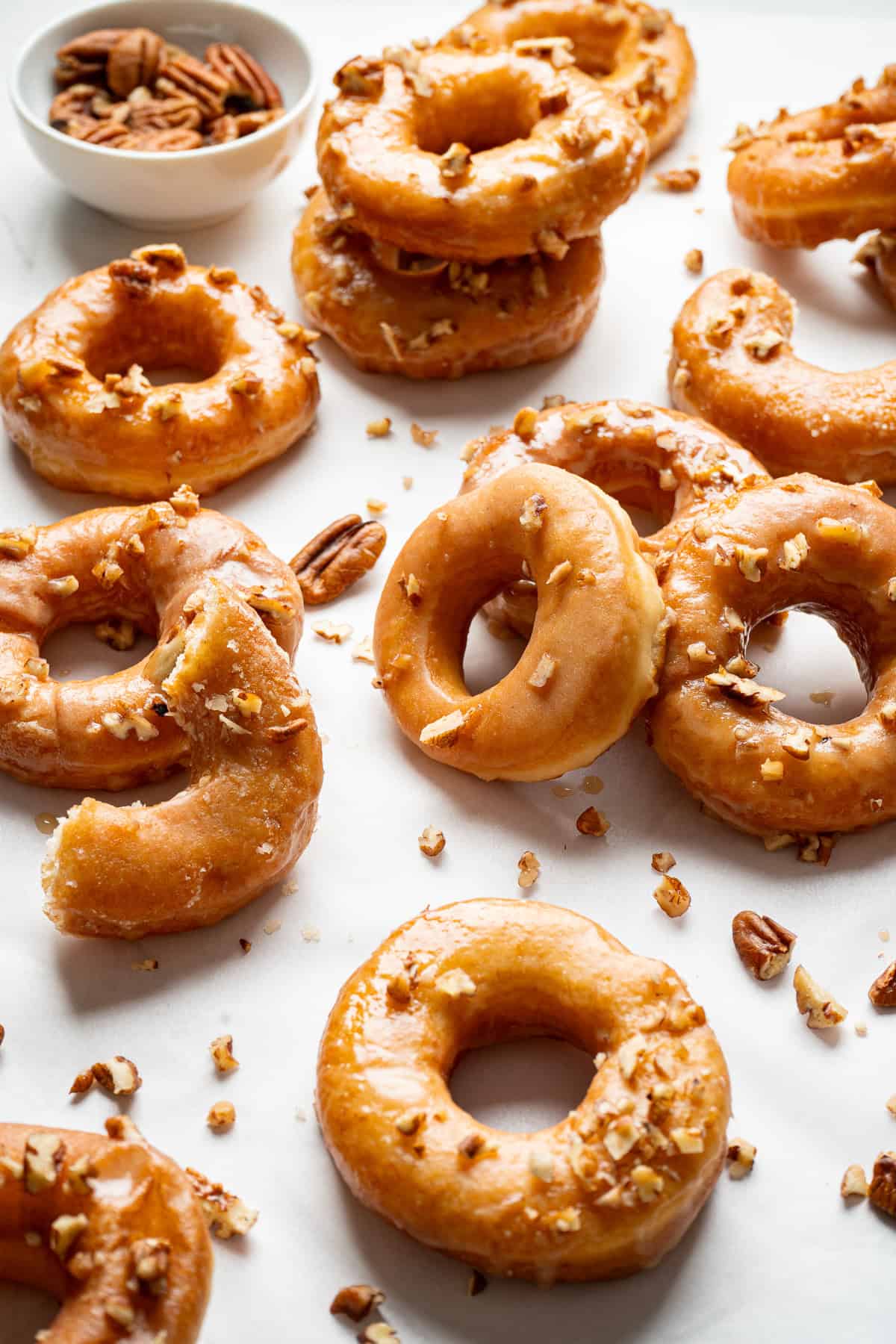 Maple glazed donuts topped with pecans, with a small bowl of pecans in the background.