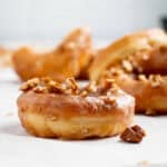 Maple glazed donuts topped with chopped walnuts on white paper.