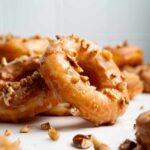 Maple glazed donuts topped with chopped nuts on a white surface.