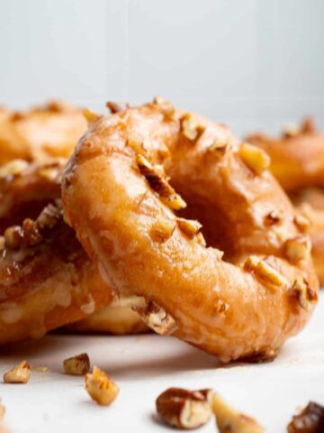 Maple glazed donuts topped with chopped nuts on a white surface.