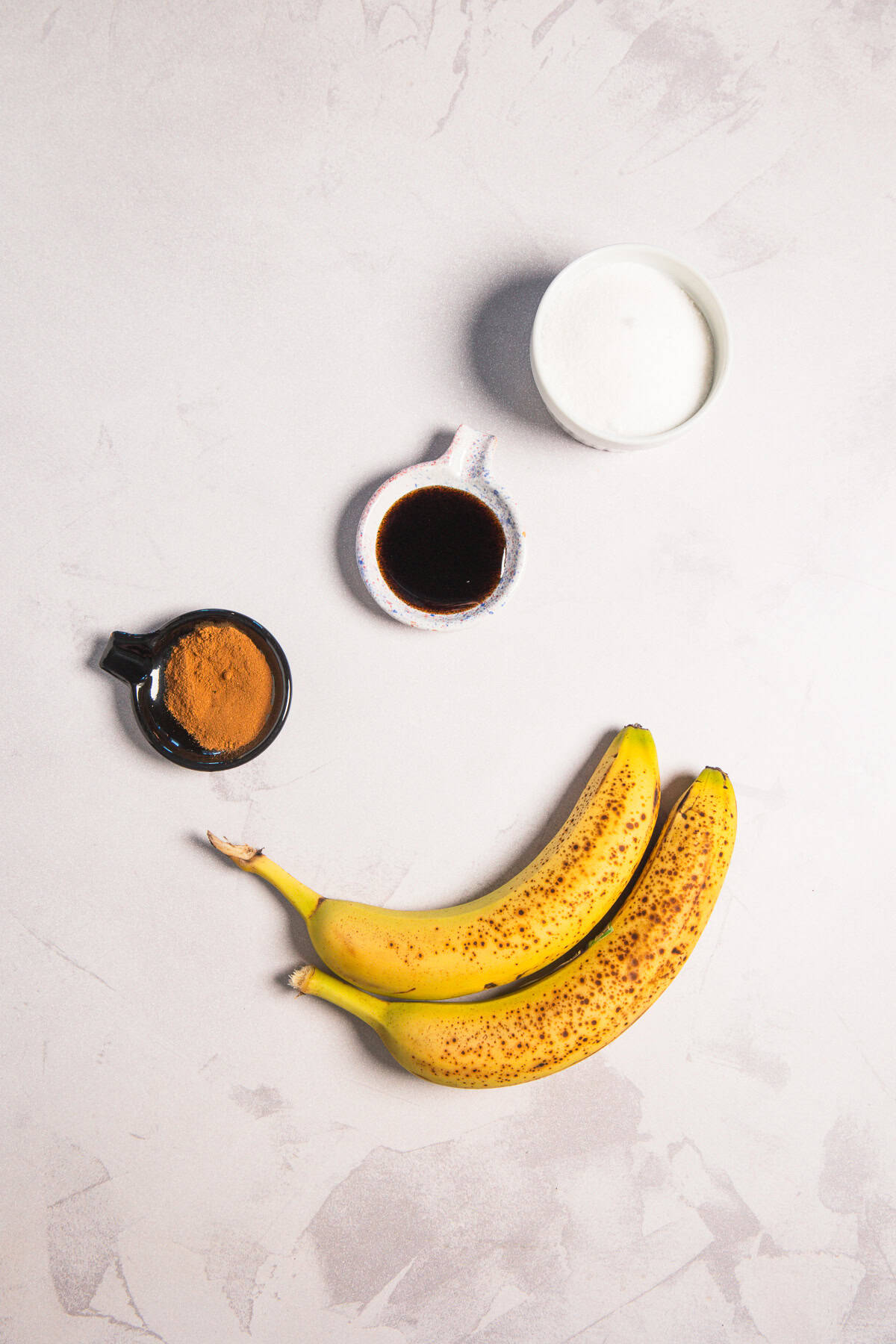Two spotted bananas, cinnamon, dark liquid, and sugar for an iced banana bread latte recipe.
