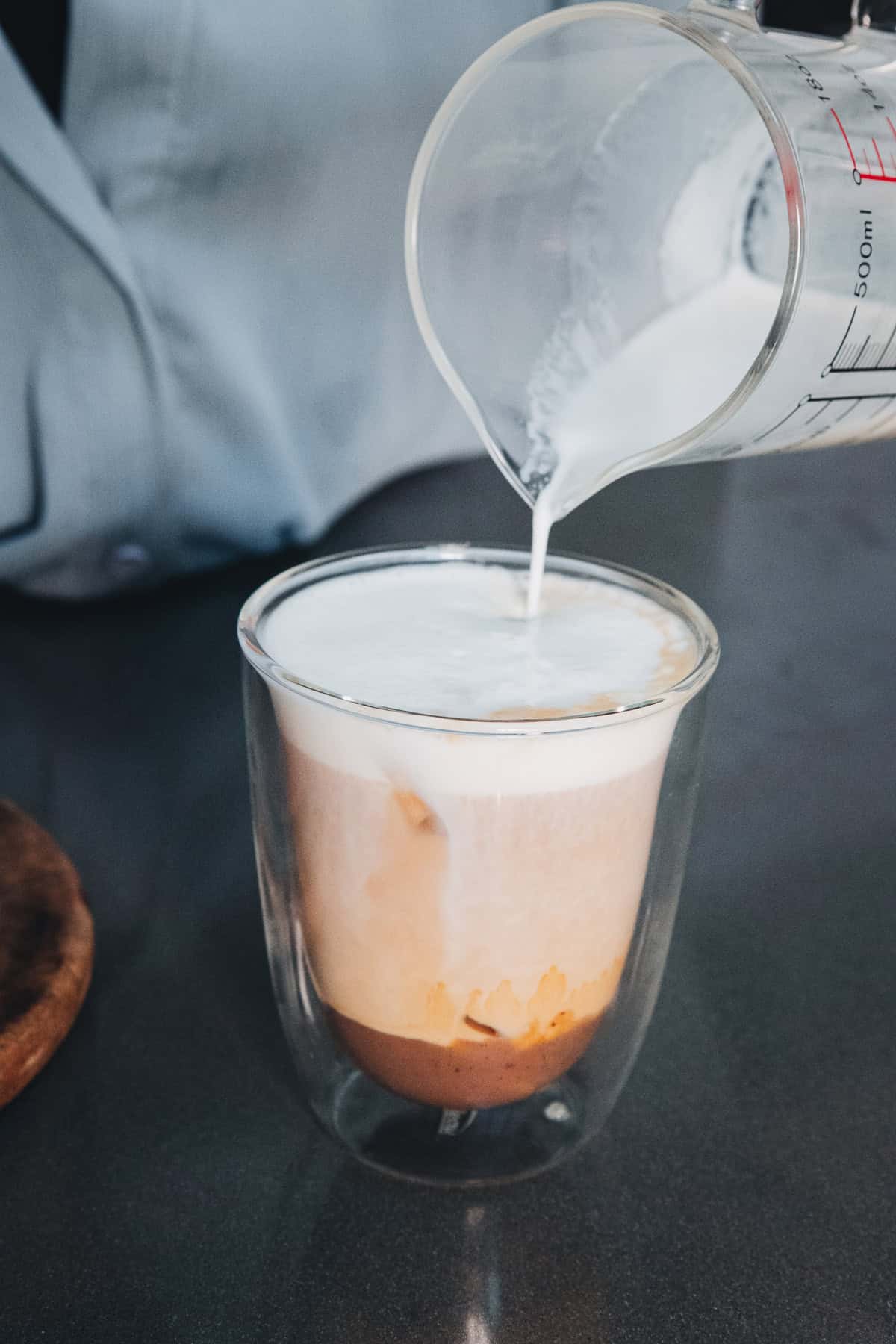 Milk being poured from a measuring pitcher into an iced banana bread latte.