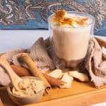 An Iced Banana Bread Latte topped with torched banana slices on a wooden tray with cinnamon, brown sugar, and crackers.